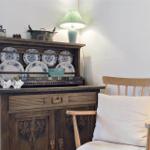 Holzschrank mit Tellern, Lampe und Stuhl mit Kissen.