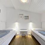 Zwei Einzelbetten, Holzboden, Fenster, weiße Wände und Decke mit eingebauten Regalen.
