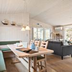Dining area with wooden table and green bench, next to living area with sofa and large windows.