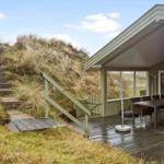Wooden terrace with table and chairs next to a house with view of dunes.