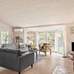 Living room with sofa, armchair, and wood stove. Large windows with view of the landscape.
