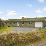 A green house with a green roof and white garage. Surrounded by grass and trees.