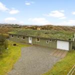 Single-story house with green roof and garage in a grassy area.