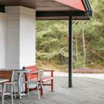 Terrasse mit Tischen, Stühlen und roter Bank. Hintergrund: Wald mit Heide.