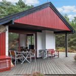 Rotes Holzhaus mit Terrasse, Tisch, Stühlen und Blick in den Wald.