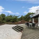 Wohnhaus mit Terrasse, Tisch und Stühlen. Umgeben von Wald und Sandfläche.