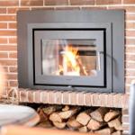 Ein Kamin mit brennendem Holz in einem Raum mit Backsteinwand und Holzstapel darunter.