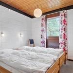Schlafzimmer mit Doppelbett, Holzboden und Fenster mit floralen Vorhängen.