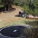 Außenbereich mit Trampolin, Holzstapel und Sitzplatz auf Terrasse.