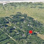 Luftbild einer Waldlandschaft mit markierter Immobilienposition und Strand im Hintergrund.