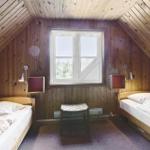 Zimmer mit zwei Betten, Holzwand und Dachschräge. Fenster mit Blick auf Bäume.
