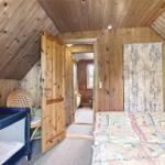 Schlafzimmer mit Holzwand, Bett, Kinderbett und Tür zu einem weiteren Raum.