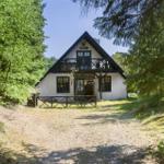 Ein weißes Haus mit dunklem Dach steht im Wald. Es hat eine Veranda und Fenster mit dunklen Rahmen.
