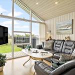 Wohnzimmer mit Ledersofa, TV und großem Fensterblick auf Grünfläche.