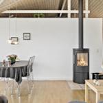 Essbereich mit Tisch, Stühlen und Kaminofen. Holzdecke und helle Wände.