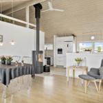 Wohnbereich mit Esstisch, Kamin und Küche. Holzboden und weiße Wände.