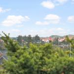 Panoramablick auf eine Siedlung mit roten Dächern und grünen Hügeln unter blauem Himmel.