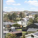 Aus dem Fenster sieht man Häuser und Grünflächen unter blauem Himmel mit weißen Wolken.