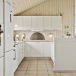 Küche mit weißen Schränken, Steinplatte und integriertem Ofen. Blick auf Wohnbereich.