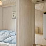 Schlafzimmer mit Bett und Holzwand. Durchgang zu einem Raum mit Schrank und Korb.