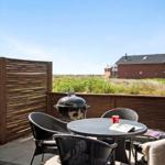 Deck with table, chairs, and grill. View of greenery and buildings.