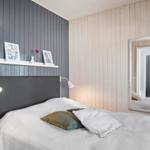 Bedroom with bed, shelf, and mirror. Wooden wall and gray wall cladding.
