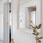 Mirror on white wall, wooden table with vase and flower, doorway to bedroom.