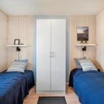 Two beds with blue bedding, white wardrobe, and wood-paneled walls.