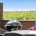 Terrace with grill, table, and chairs. View of green areas and horizon.