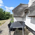 Terrasse mit Tisch und Stühlen neben einem Haus mit Strohdach.