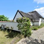 Wohnhaus mit Strohdach, gepflasterter Weg und Blumenbeet. Fahrrad an der Wand.