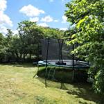 Hinterhof mit Trampolin, Sitzgelegenheiten und Bäumen unter blauem Himmel.
