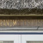 Holzschild mit der Aufschrift STRANDMARKSHUSET unter einem Strohdach.