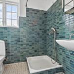 Badezimmer mit Badewanne, Toilette und Waschbecken. Wände mit blauen Fliesen.