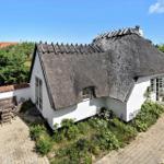 Haus mit Strohdach, Terrasse und Garten. Weiße Wände, Holzmöbel und Pflanzen.