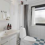 Badezimmer mit Toilette, Waschbecken und Dusche. Fenster mit weißen Vorhängen.