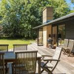 Terrasse mit Holztisch, Stühlen und Grill. Hintergrund: grüner Rasen und Bäume.