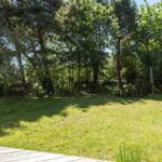 Grüner Garten mit Holzbank und Sonnenschutz unter Bäumen. Blick von einer Terrasse.