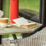 Auf dem Balkon steht ein Tisch mit Buch, Tasse und rotem Thermobecher.