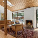 Wohnzimmer mit Kamin, Holzdecke und Glasfront zur Terrasse.