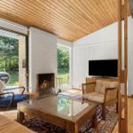 Wohnzimmer mit Kamin, Fernseher und großem Fensterblick auf Garten.