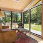 Wohnbereich mit Sitzgruppe, Tisch und Blick auf Garten durch große Fenster.