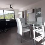 Essbereich mit Glas-tisch und weißen Stühlen. Wohnbereich mit Sofa und Aussicht.