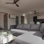 Wohnzimmer mit Sofa, Glas-Tisch und TV. Küche mit Küchenschränken und Arbeitsplatte.