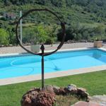 Pool mit Steinumrandung und Skulptur im Vordergrund. Grüne Landschaft im Hintergrund.