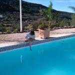 Person sitzt am Poolrand mit Blick auf Hügel und Palmen.