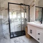 Badezimmer mit marbliertem Boden und Wand, Dusche mit Glaswand und Waschtisch mit Spiegel.