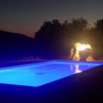 Beleuchteter Pool bei Nacht mit Feuerfontäne im Hintergrund.