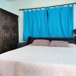Schlafzimmer mit Bett, dunklem Schrank und blauen Vorhängen.