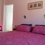 Schlafzimmer mit Bett, Kissen und Wandbild. Rote Sitzgelegenheit und angrenzender Flur.